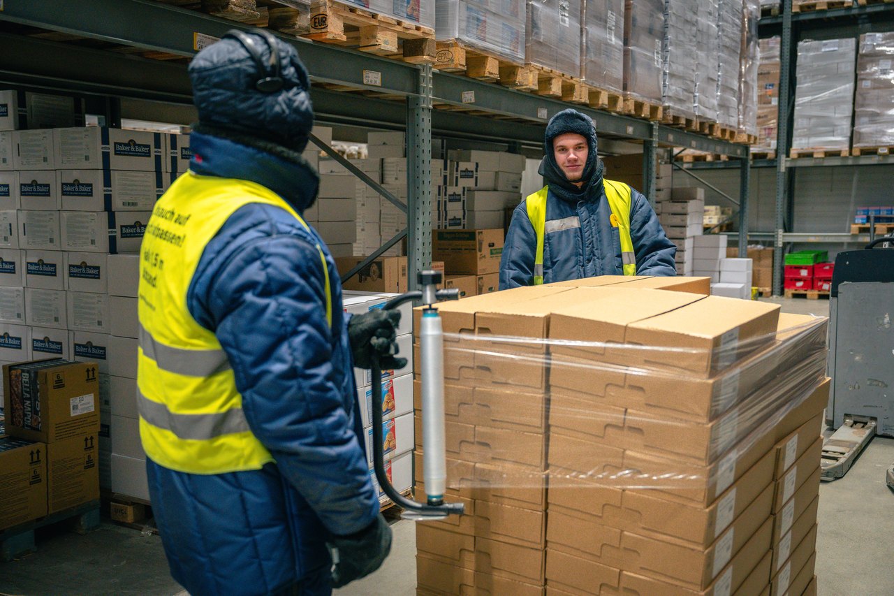 Zwei Lagerarbeiter verpacken Kartons mit Schrumpffolie in einem gekühlten Lager.